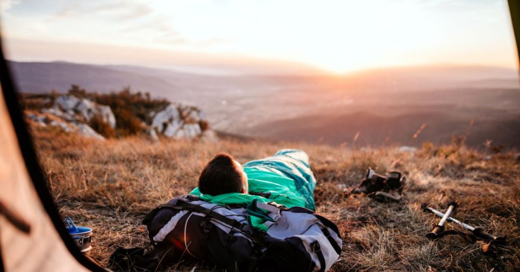 camper in sleeping bag lying down facing the sunset